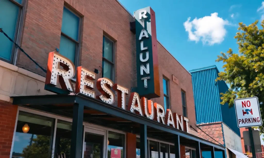 Exterior view of a brick restaurant building with a retro-style "Restaurant" sign under a sunny blue sky.
