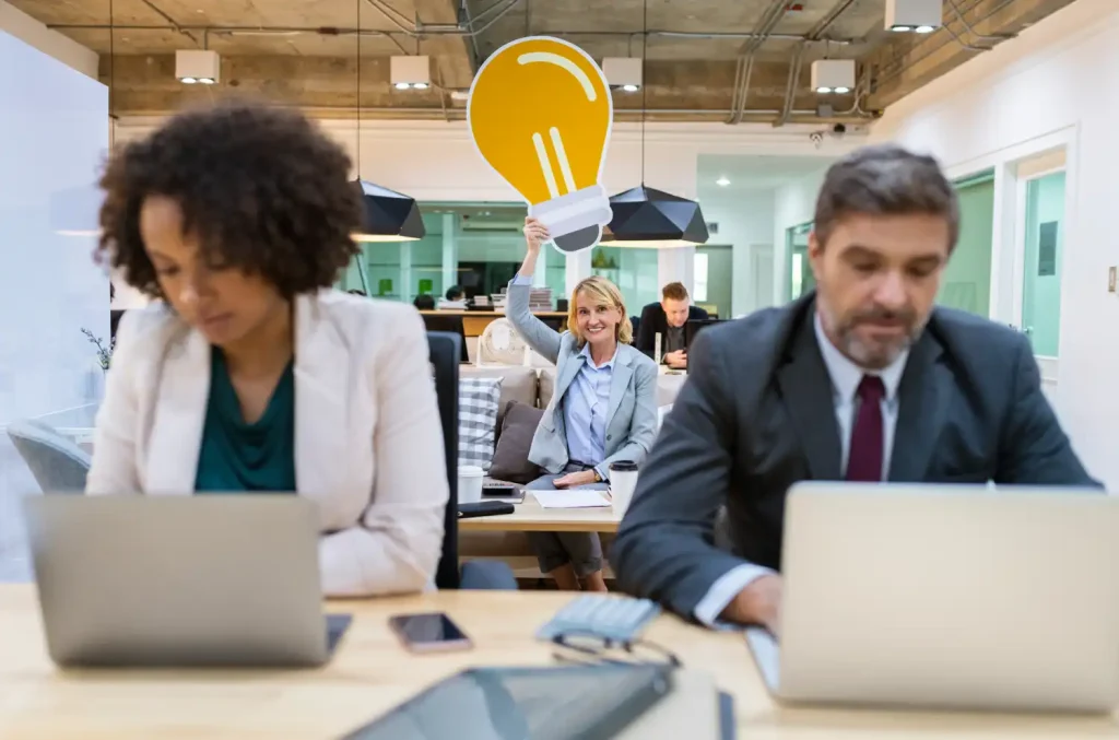 Businesswoman holding a large lightbulb cutout behind coworkers in an office.
