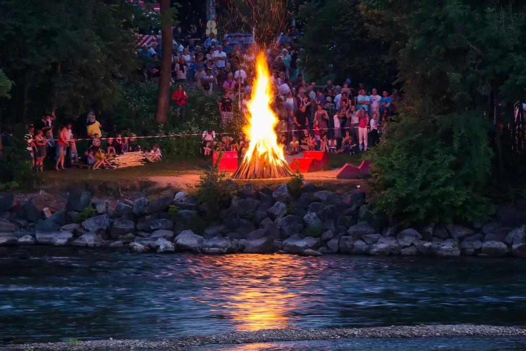 Bonfire surrounded by people celebrating near a riverside.