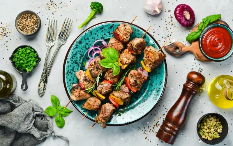Grilled Persian kebabs served on a turquoise plate with fresh herbs and colorful vegetables.