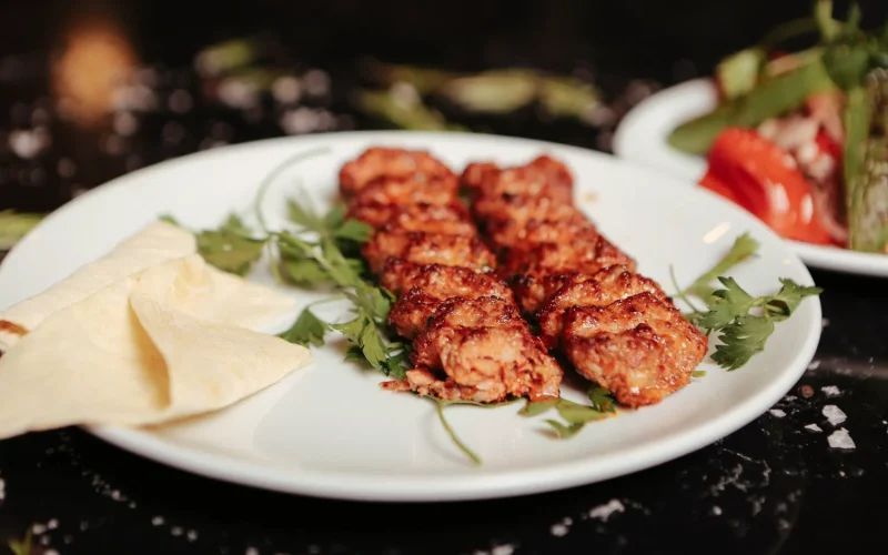 What Makes Iranian Cuisine Unique? Juicy grilled kebabs served with fresh herbs and flatbread on a white plate.