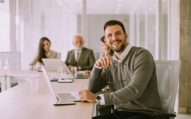 Smiling businessman sitting at a desk with a laptop during a meeting.