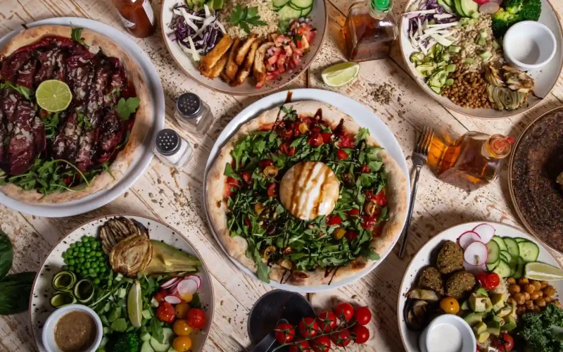 A spread of Middle Eastern and Persian-inspired dishes including salads, pizzas, and falafel with colorful garnishes.