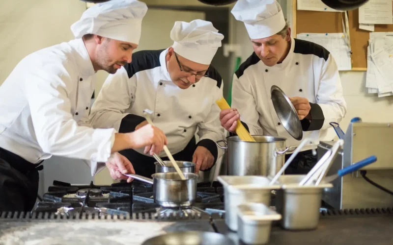 Chefs in white uniforms collaborating in a professional kitchen while cooking.