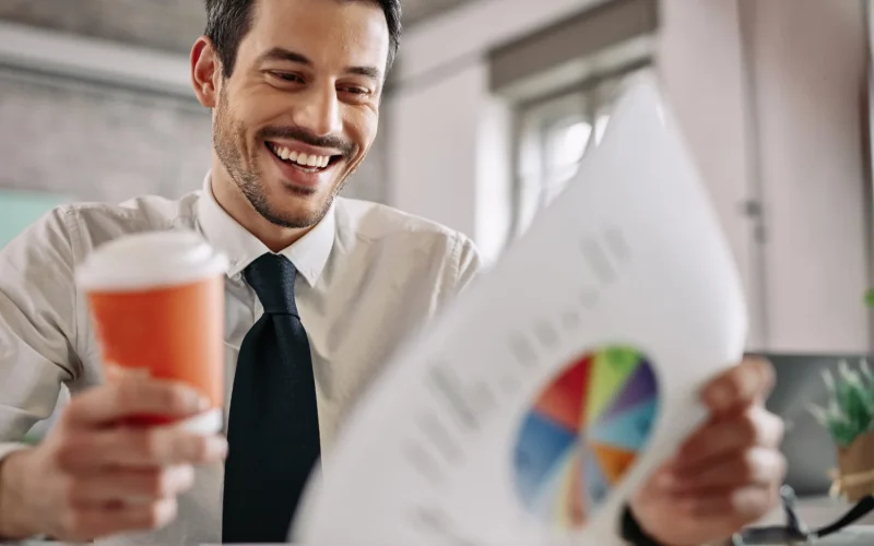 Smiling businessman reviewing a colorful chart while holding a coffee cup.