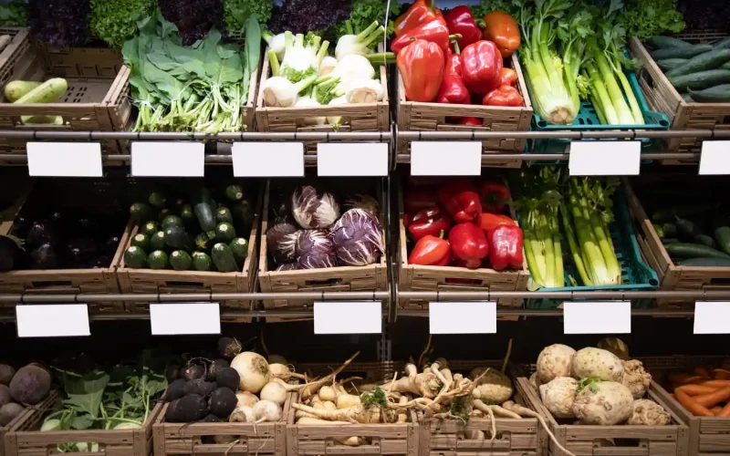 Fresh produce, including peppers, celery, zucchini, and root vegetables, displayed in wooden crates at a grocery store.