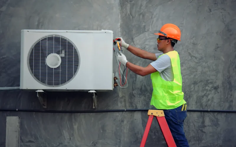 HVAC technician in safety gear performing maintenance on an outdoor air conditioning unit.
