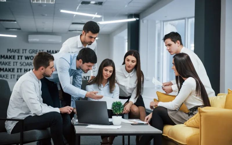 A group of professionals collaborating around a laptop in a modern office setting.