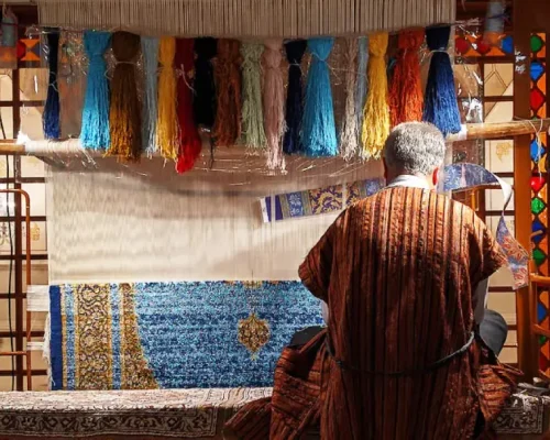 Artisan weaving a traditional Persian rug on a loom, surrounded by colorful threads.