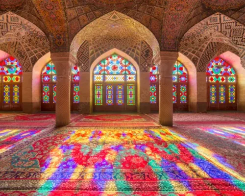 Nasir al-Mulk Mosque interior with vibrant stained glass windows casting colorful patterns on Persian carpets.