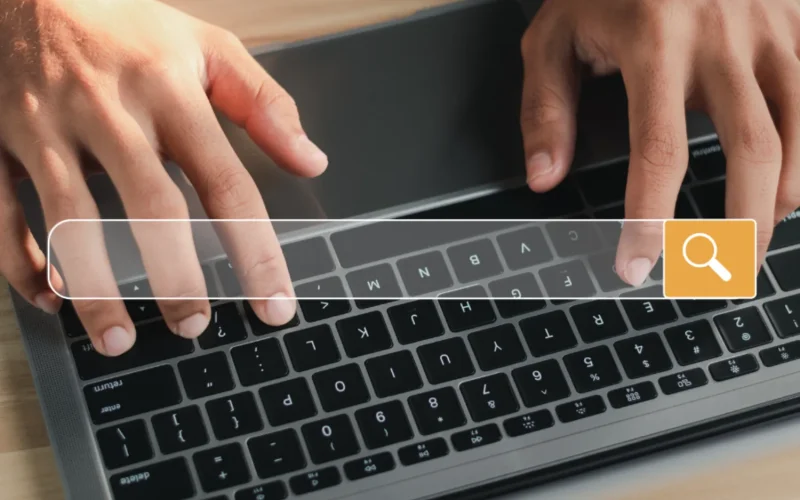 Hands typing on a laptop with a search bar.