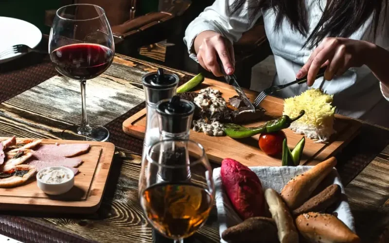 A person dining on traditional Iranian food with wine and bread on a rustic wooden table.