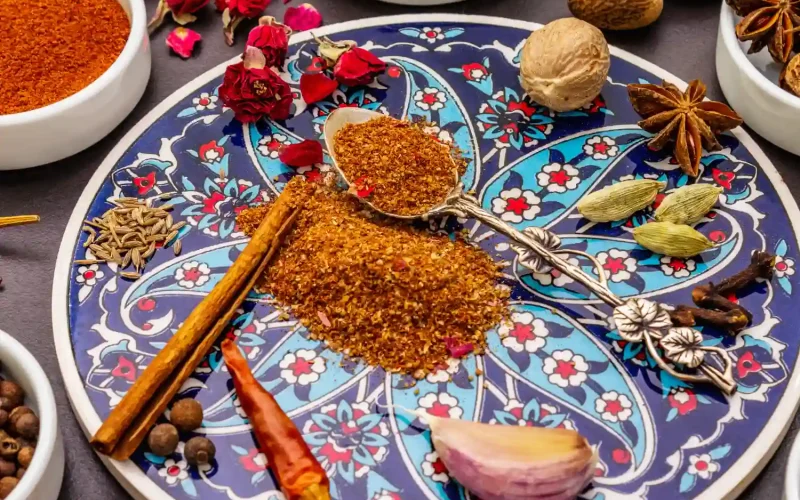A decorative Persian plate featuring aromatic spices like cinnamon, cardamom, cloves, and dried rose petals.