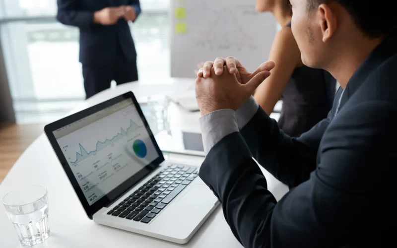 Business professionals discussing growth strategies with analytics displayed on a laptop screen.