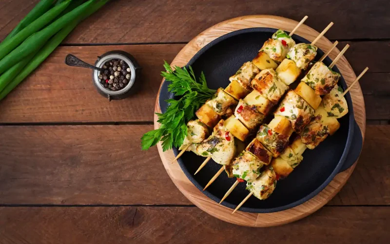 Grilled chicken and vegetable skewers served on a black plate with fresh parsley garnish.